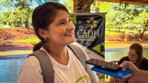 Mulher de camiseta branca e mochila nas costas dá entrevista.